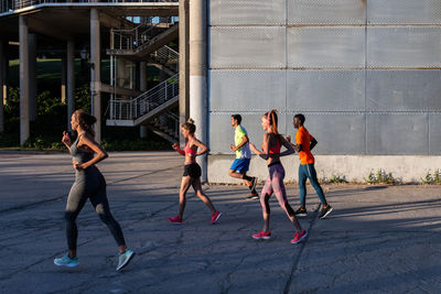 Side view of diverse sportspeople running along street while training together in city on sunny day