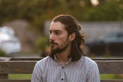 Portrait of young man with long hair looking away outdoors