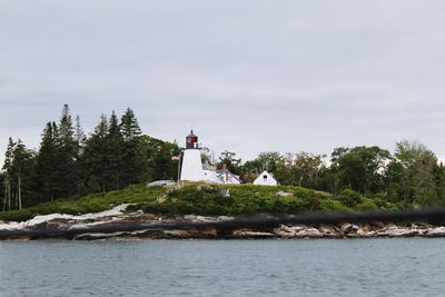 Lighthouse by lake and building against sky