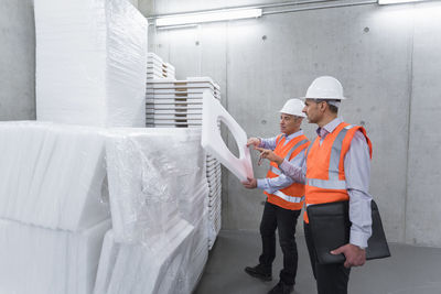 Two colleagues wearing safety vests and hard hats examining polystyrene