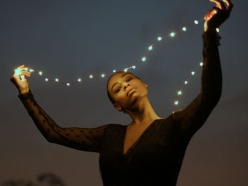 Midsection of woman holding illuminated lighting equipment against sky