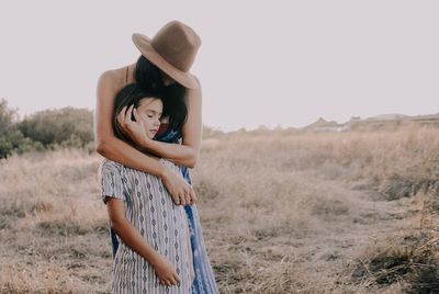 Young woman standing on field with arms wrapped around her daughter in an embrace 