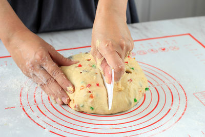 Baker hand cuts raw yeast fruit bread dough on white table background with a plastic knife. 