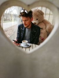 Man using mobile phone while sitting at table in cafe seen through heart shape