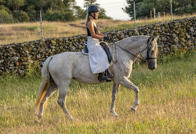 Lusitano horse, white mare, female rider, outdoors on pasture.