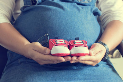 Midsection of pregnant woman holding baby shoes