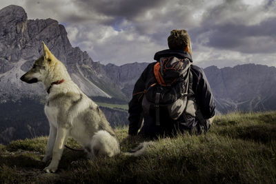 Rear view of dog sitting on field against sky