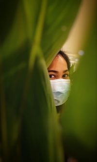 Close-up portrait of woman wearing mask seen through leaves