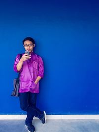 Portrait of young man wearing eyeglasses standing against blue wall