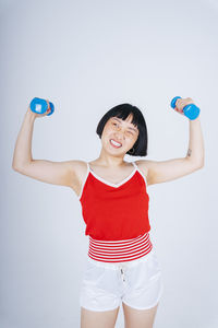 Young woman exercising with dumbbell against gray background