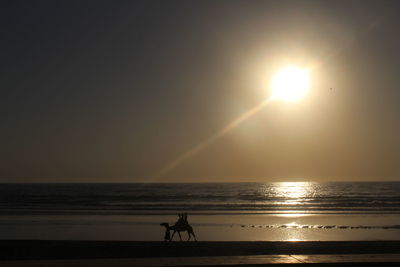 Silhouette people at beach against clear sky during sunset