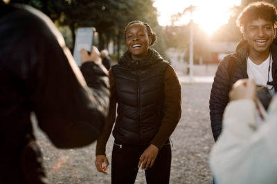 Friends filming smiling teenage girl and boy dancing on street in city