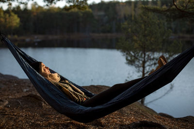 Young woman sleeping on hammock at lakeshore during sunset