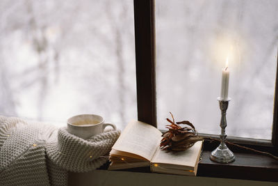 Cup of hot tea and an open book with a warm sweater on a vintage wooden windowsill