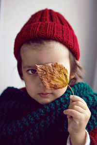 Boy child in red knitted sweater and hat sitting on the window in autumn