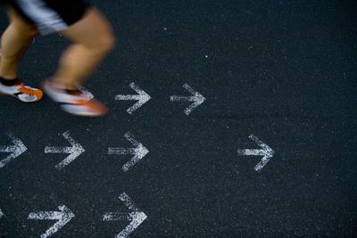 Low section of person running on street with arrow signs