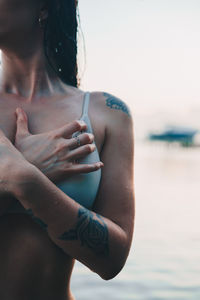 Midsection of shirtless woman in sea against sky