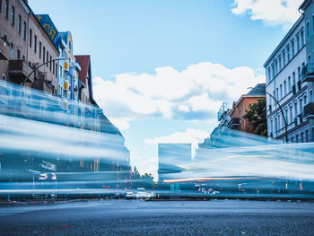 Light trails on street by buildings against sky in city