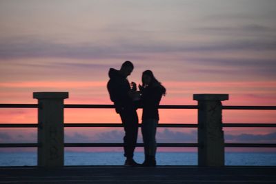 Silhouette couple standing by sea against sky during sunset