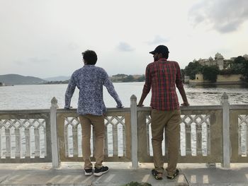 Rear view of men looking at lake while standing by railing against sky