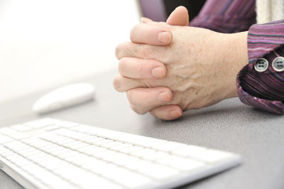 Cropped image of person with hands clasped by computer keyboard on table