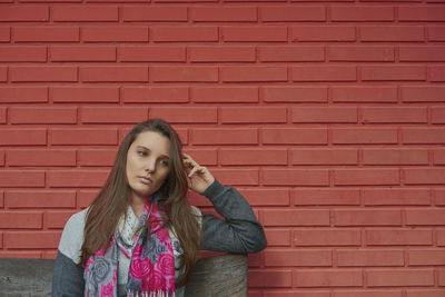 Thoughtful young woman standing against brick wall