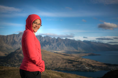 Portrait of smiling woman standing on hill by lake at queenstown