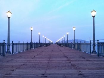 Empty street lights on pier against sky at dusk