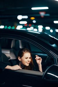 Happy young woman looking in side-view mirror of car