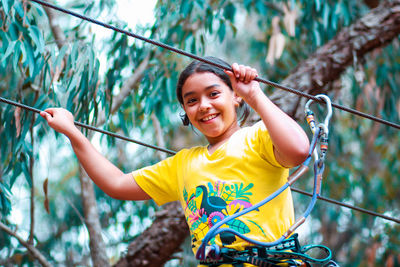 Portrait of smiling girl holding rope against trees