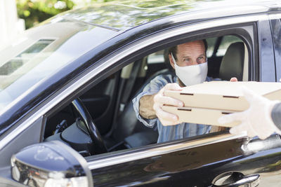 Man in fabric mask receives pizza through curbside pickup