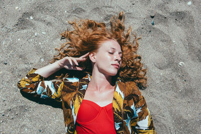 High angle view of young woman with eyes closed lying on sand