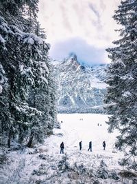 People on snow covered field by rocky mountains against sky