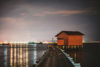 Illuminated building by river against sky at night