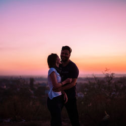 Happy couple standing on field during sunset