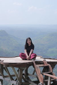 Portrait of young woman sitting on mountain against sky