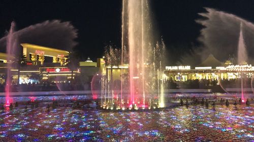 Illuminated fountain in lake against sky at night