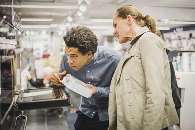 Mature customer and young salesman looking at oven in electronics store