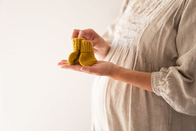 Midsection of pregnant woman holding newborn socks against white background