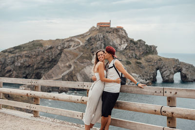 Couple standing by railing against sea and rock formation