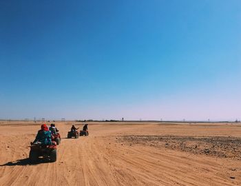 People on buggies in desert against clear sky