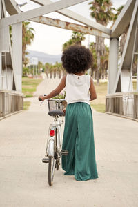 Afro woman with bicycle walking on bridge