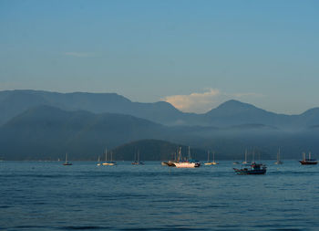 Sailboats in sea against mountains