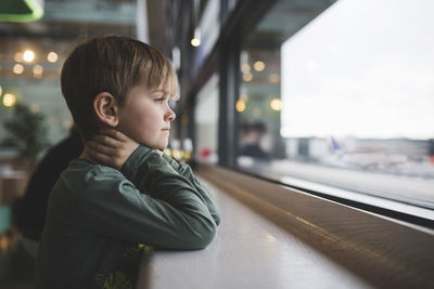 Thoughtful boy leaning on table by window of restaurant