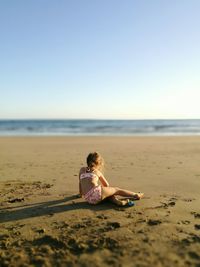 Full length of girl sitting on beach against sky