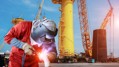 Low angle view of man working at factory against sky