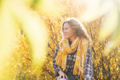 Young beautiful woman with curly hair in plaid shirt, jeans and yellow scarf on yellow tree 