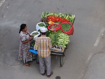 High angle view of woman buying vegetables on cart from male street vendor in city