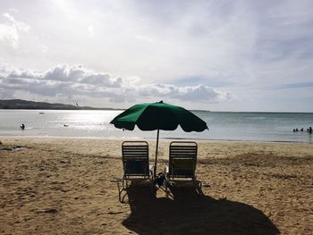 Lounge chairs and umbrella at beach against sky on sunny day