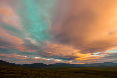 Scenic view of landscape against dramatic sky during sunset